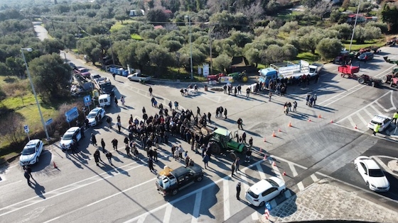 Τα οχήματα των αγροτών παραμένουν σταθμευμένα στον κόμβο, υποδηλώνοντας την αποφασιστικότητα των συμμετεχόντων να συνεχίσουν τις κινητοποιήσεις τους.